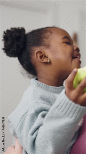 Cute little african american girl with a fun hairstyle biting and eating a juicy green apple. Healthy snack for children's nutrition. Vertical