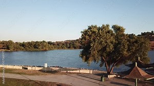gorgeous footage of a vast rippling blue lake at sunset surrounded by majestic mountain ranges covered in lush green trees and plants with blue sky at Puddingstone Lake in San Dimas California USA Stock Video