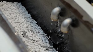 Tumble finishing process at factory: automated trough vibrator machine polishing metal workpieces by abrasive stones: close up, slow motion. Metalworking, industrial, technology, manufacturing concept