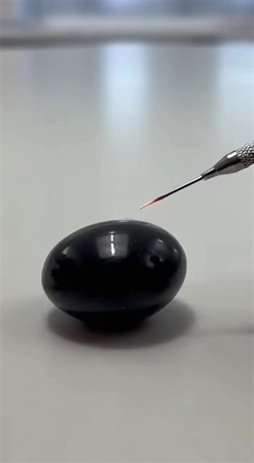 A cold, glassy shell is precisely scored and split, releasing a shimmering, sticky core — the payoff is the intimate contrast between brittle crack and glossy stretch.