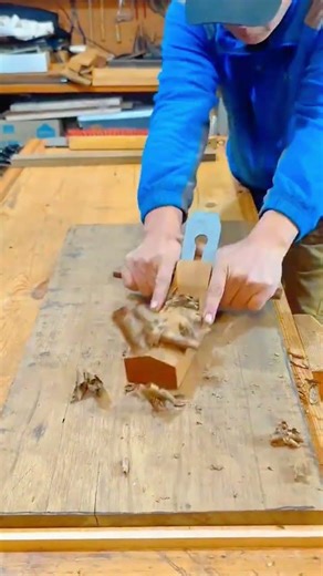 Smoothing the surface of a wide wooden board using a manual hand plane tool on a large workbench