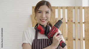 Beautiful Asian female carpenter woodwork stands tall, showing off a cordless drill. Owner business, Small business.
