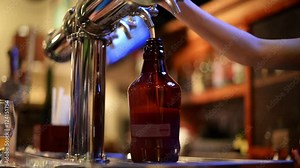 Close up bartender fills a growler from beer tap.