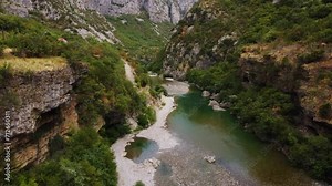Aerial drone view of suspension old metalic bridge in the middle of beautiful rocky canyon with turquoise river, Montenegro. Moraca river canyon with green vibrant vegetation