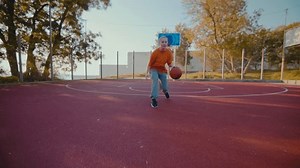 Young woman athlete bounces ball passing to teammates on city playground at sunset. Athletic young female in sportswear shows professional skills in sports