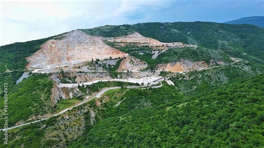 Natural quarry is located near road against backdrop of Rhodope Mountains and hills with forests and mountain vegetation