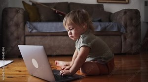 Toddler is sitting in front of a laptop. Funny little kid is working on a laptop at home. The concept of learning, parenting, childhood, working remotely, programming