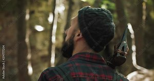 Walking bearded lumberjack with axe. Man in a cap walks through the woods in search of the tree. View behind the back
