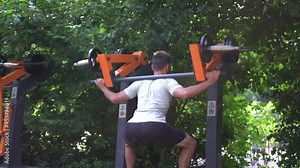 Man doing squats using outdoor training machine. Open air training.