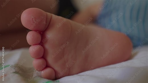 Close up baby foot resting on bed sheet with soft skin texture and tiny toes, intimate detail of newborn body expressing innocence vulnerability warmth and early life