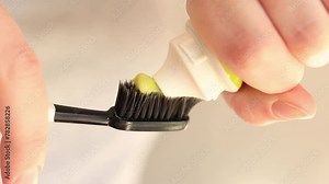 Squeezing toothpaste onto a toothbrush, close-up. Brushing your teeth. Healthcare, oral hygiene. A woman squeezes white toothpaste from a tube onto a black toothbrush. Morning hygiene procedures