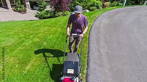 Adult male mowing the lawn in front of his American suburban home with a push mower