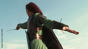 A fierce medieval warrior woman draws her sword from its sheath and points it forward, commanding her troops to charge into battle.