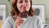 Happy young woman eating chocolate at home