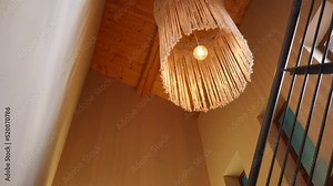 Bottom angle view of lamp hanging in fabric lampshade on ceiling indoors. Cozy decoration above stairs in tourist resort hotel with no people