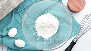 Making a dessert called Red Raspberry Tea Cake made with fresh berries and vanilla buttercream frosting. Great for Tea Parties. Adding regular flour into the mixing bowl and combining the ingredients.