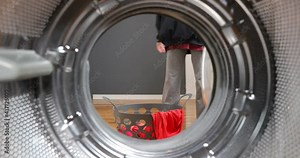 View Looking Out From Inside Washing Machine. Dirty clothes falls to a laundry basket. Housewife loading and turning on washing machine. Family carrying clothes into the laundry basket.