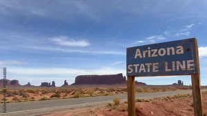 Primitive Wooden Arizona State Line Sign on the edge of Monument Valley Navajo National Land with beautiful sandstone buttes and empty road in the background - Arizona, USA