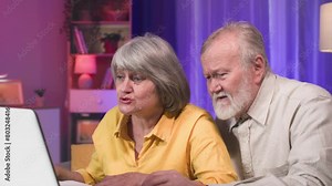 entertaining elderly people, happy female and male pensioners having fun playing modern games on laptop at home