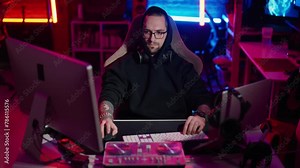 Hacker writing code cracking computer. Man programmer in hoodie cracks system, using computer in dark room. Hacker attack, technology, virus infected software, dark web, cyber security concept.