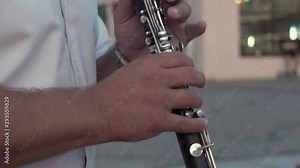 Musician in a white shirt plays the clarinet. Pan up. Street performance.