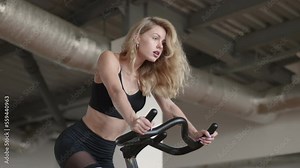 Caucasian girl in her 30s hitting the gym for an improvement her aerobic capacity. Pretty, athletic woman exercising on the stationary bike. High quality 4k footage