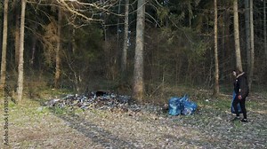 A woman throws out garbage in a bag in the forest near an unauthorized dump.