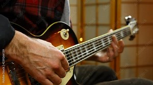 Man tuning his guitar with harmonics. Wide, fixed scene, focus on the right hand