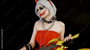 Angry evil devil girl with horns grins, want to kill, murder, leads thumb along the neck, wicked smile. Celebrate halloween with scary pumpkins on dark black background in smoke