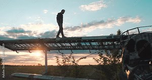 Curious bearded tourist walks along the huge wing of an abandoned corn plane in deserted grass field against the backdrop of the sunset in slow motion. Tour of the old Soviet aircraft at the airport.