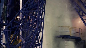 A closeup of the details of the launch pad construction where the rocket is installed. Puffs of steam come from the rocket. Night shooting.