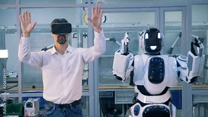 A human-like robot and a man are synchronically moving different parts of their bodies