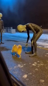 The landing site is quiet as two alien figures step away from their craft. Nearby, a dog notices them and immediately moves closer. Instead of fear, its reaction is unexpected. The dog wags its tail, bouncing lightly from side to side, curious and playful. It circles the aliens, lowering its head and making small, excited movements, as if inviting them to play. The aliens pause, watching the animal’s behavior with interest, unsure how to respond. The moment feels oddly warm and surreal, like a s