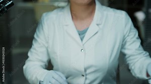Midsection shot of female forensic technician putting on sterile gloves, then taking lighted magnifying glass and examining evidence in plastic container in crime laboratory