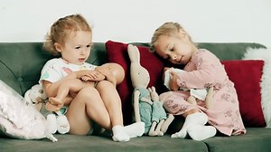 Little girls play with dolls on the sofa at home
