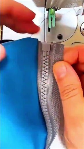 attaching a gray plastic zipper onto a blue fabric edge precisely using an industrial sewing machine