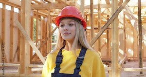 portrait of a blonde happy female engineer smiling looking at camera, having rest working on a construction site. wooden build manufacturing in the background job profession occupation lifestyle