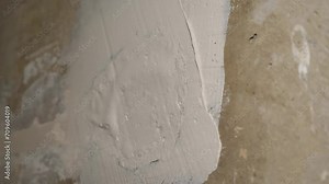 A plasterer applies putty or plaster to a wall using a putty knife. A man seals an electrical distribution box with gypsum plaster mortar. Finishing walls before painting or wallpapering.
