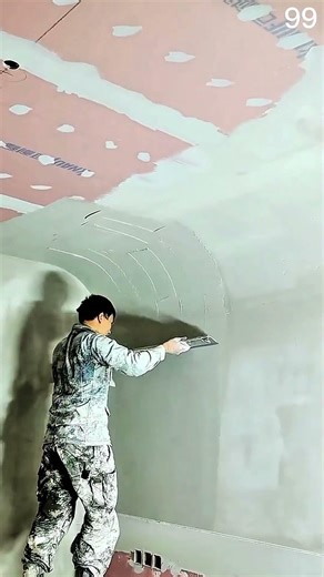 Worker applies joint compound on curved ceiling edge
