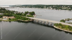 Aerial view of coastal town flying over bridge to see sail boats in harbor in New England