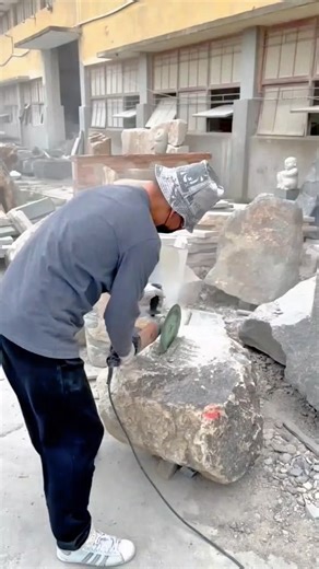 Cutting and shaping a large stone block using an electric grinder at a stone workshop