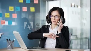 Angry businesswoman arguing on phone seen in modern office. Professional woman in suit frustrated during stressful work discussions. Businesswoman expressing anger and stress using laptop in workplace