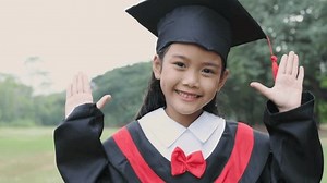 Educational concept of 4k Resolution. Asian girl in graduation gown doing peek-a-boo pose in the garden.