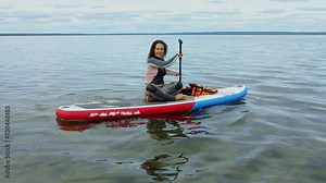 Woman in surfer suit sculls on inflatable SUP board by water. Slow motion