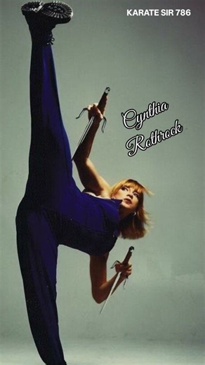 This image features martial artist and actress Cynthia Rothrock, known as the "Queen of Martial Arts". Rothrock held black belt rankings in seven different styles of martial arts. She maintained an undefeated worldwide record in martial arts forms competition from 1981 to 1985. Born on March 8, 1957, in Wilmington, Delaware, she became a prominent figure in martial arts films. The image showcases her impressive flexibility and skills with weapons like hookswords. | KARATE SIR