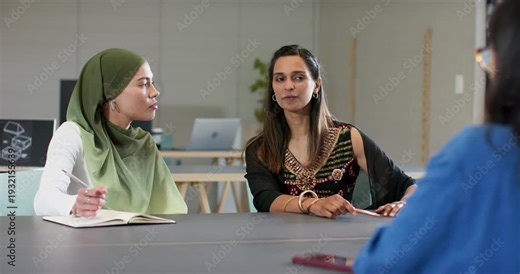 Off-screen colleague gesturing to Indian women jotting notes in notebook and speaking in meeting