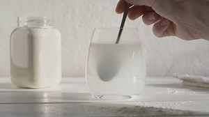 Putting a spoon of whey protein powder into a glass of water and stirring it, slow motion