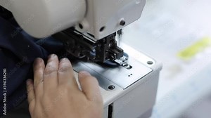 The worker is sewing a textile with a sewing machine in a fabric factory.
