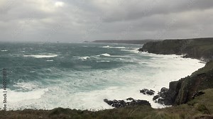 Stormy rough seas and breaking Atlantic ocean waves over rocks at Lands End Cornwall, UK after Storm Bella gale force winds surge through the coastline.