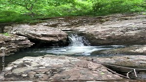 Pure mountain stream - a waterfall flows in the middle of a green forest, between huge boulders. Moss-covered gray boulder stones